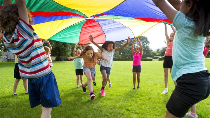Group of children playing outside with a parachute.