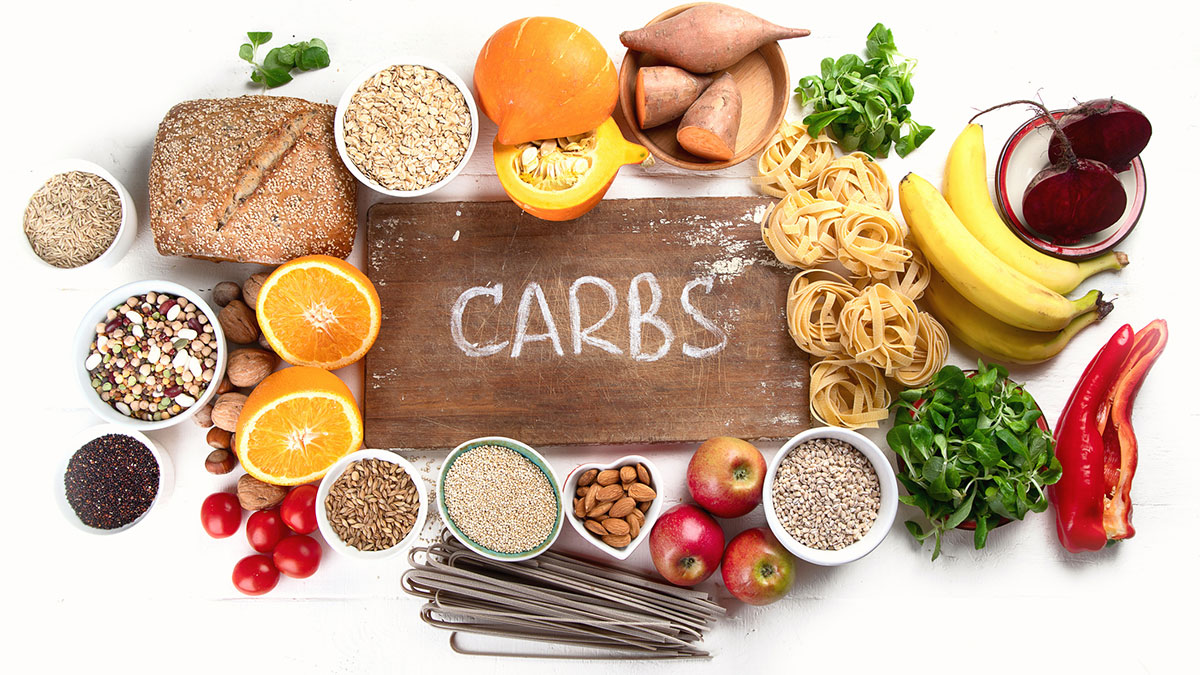 Wooden sign with the word "carbs" surrounded by various carbs discussed in the article