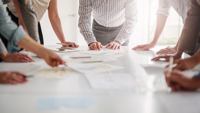 View of hands of multiracial group of people working with ideas together to make decisions with documents on table.