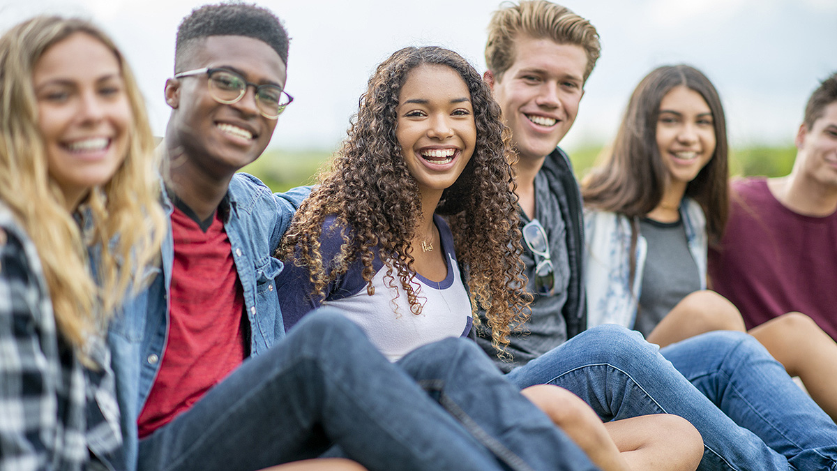Diverse group of young adults sitting in a line and embracing outside.